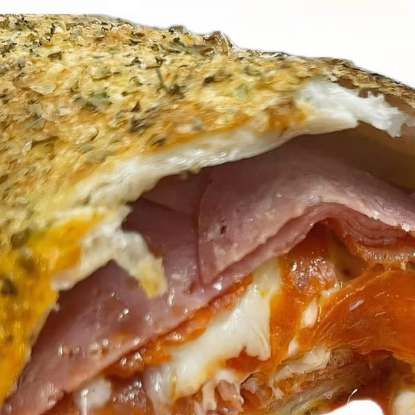 Close-up of a Freshieez calzone, revealing layers of ham, pepperoni, and melted cheese inside.