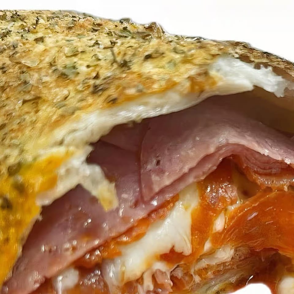 Close-up of a Freshieez calzone, revealing layers of ham, pepperoni, and melted cheese inside.