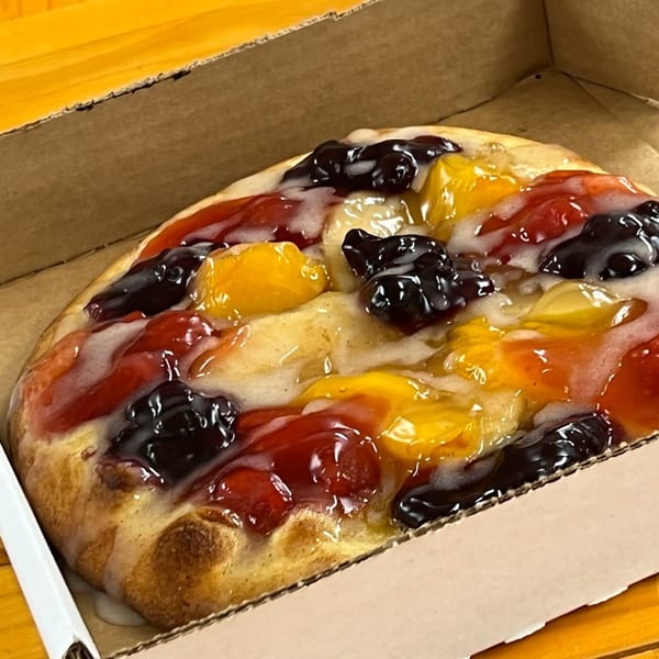 Freshieez dessert pizza with colorful fruit toppings and white icing in a cardboard box.