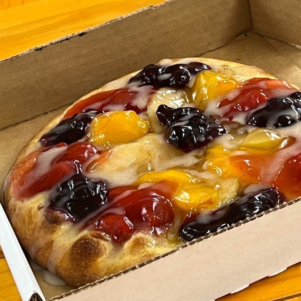 Freshieez dessert pizza with colorful fruit toppings and white icing in a cardboard box.
