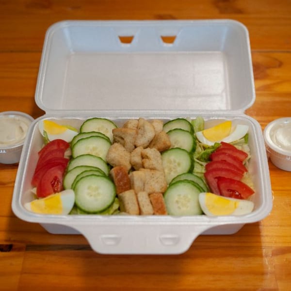 Freshieez garden salad with cucumbers, tomatoes, croutons, and hard-boiled eggs in a takeout container.