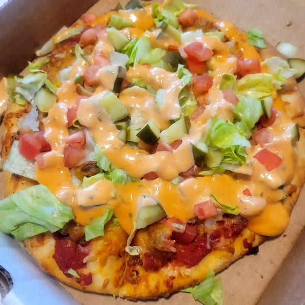 Freshieez pizza topped with lettuce, diced tomatoes, pickles, and a creamy orange sauce.