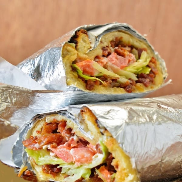 Two Freshieez pizza wraps, filled with meat, lettuce, and sauce, partially unwrapped from foil.