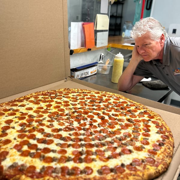 Man intently looking at a giant pepperoni and sausage pizza in an open box.